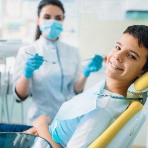 Smiling little boy in a dental chair, professional pediatric dentistry, children stomatology, female dentist on background